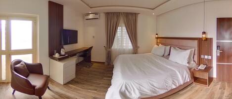 Ein Hotelzimmer mit einem großen Bett, einem Schreibtisch mit Stuhl, einem Fernseher und einem Telefon auf einem Nachttisch.