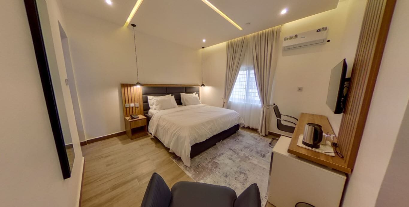 Una habitación de hotel moderna con una cama grande, mesitas de noche, un escritorio con silla, un televisor y una ventana con cortinas.