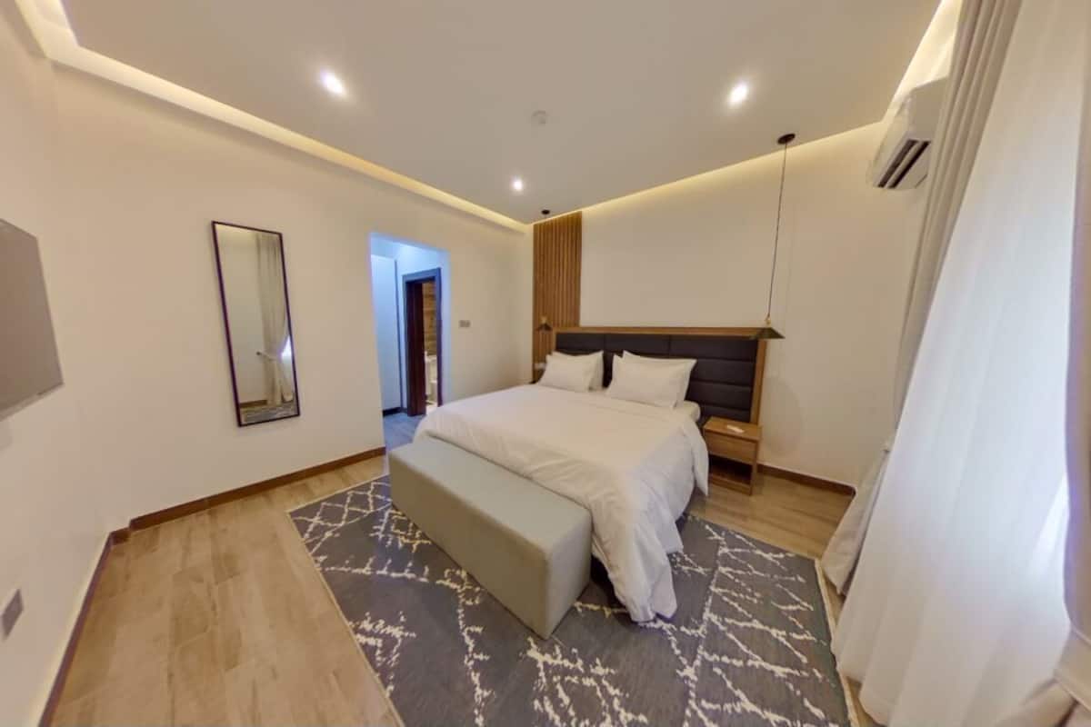 Una habitación de hotel moderna con una cama grande, mesitas de noche, un televisor de pantalla plana y un espejo.