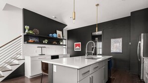A modern kitchen with a central island, stainless steel appliances, and a black accent wall. - Arch One ~ Joint Listing ~ Two Units ~ 24 Beds in Gulch ~ Free Parking ~ Eight Clean Private Suites (Nashville)