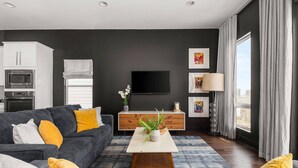 A modern living room with a grey sofa, yellow cushions, a white coffee table, and a large window with curtains. - Arch One ~ Joint Listing ~ Two Units ~ 24 Beds in Gulch ~ Free Parking ~ Eight Clean Private Suites (Nashville)
