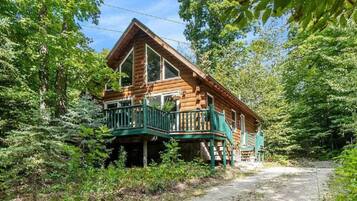A log cabin with a balcony, surrounded by dense forest.