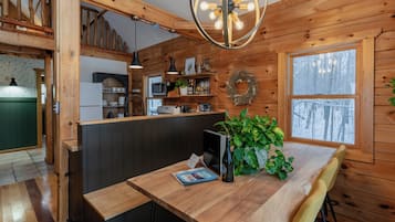 A wooden interior with a wooden table, a potted plant, and a view of the outdoors through a window.