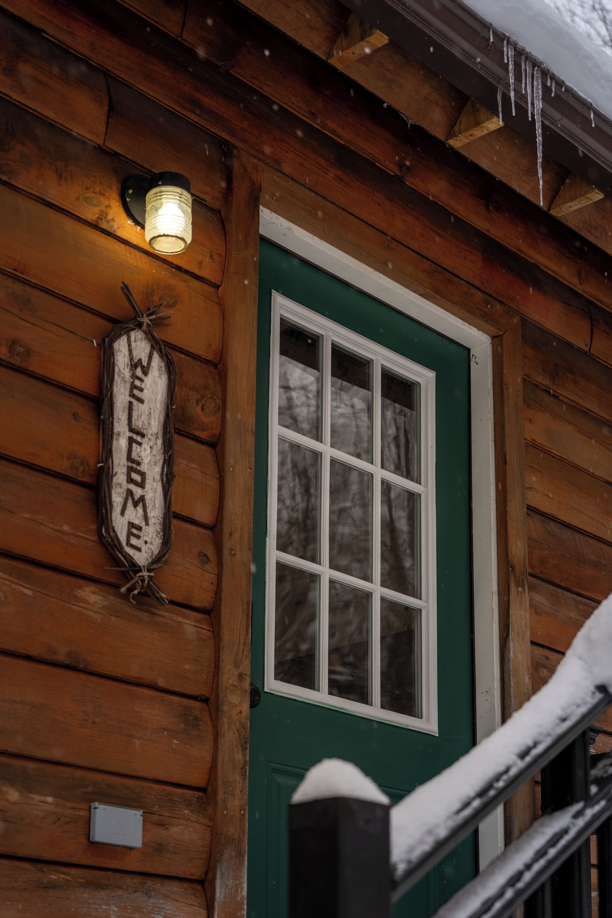 Eine Holzhütte mit grüner Tür, einem Willkommensschild und einem Fenster.