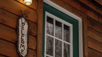 A wooden cabin with a green door, a welcome sign, and a window.