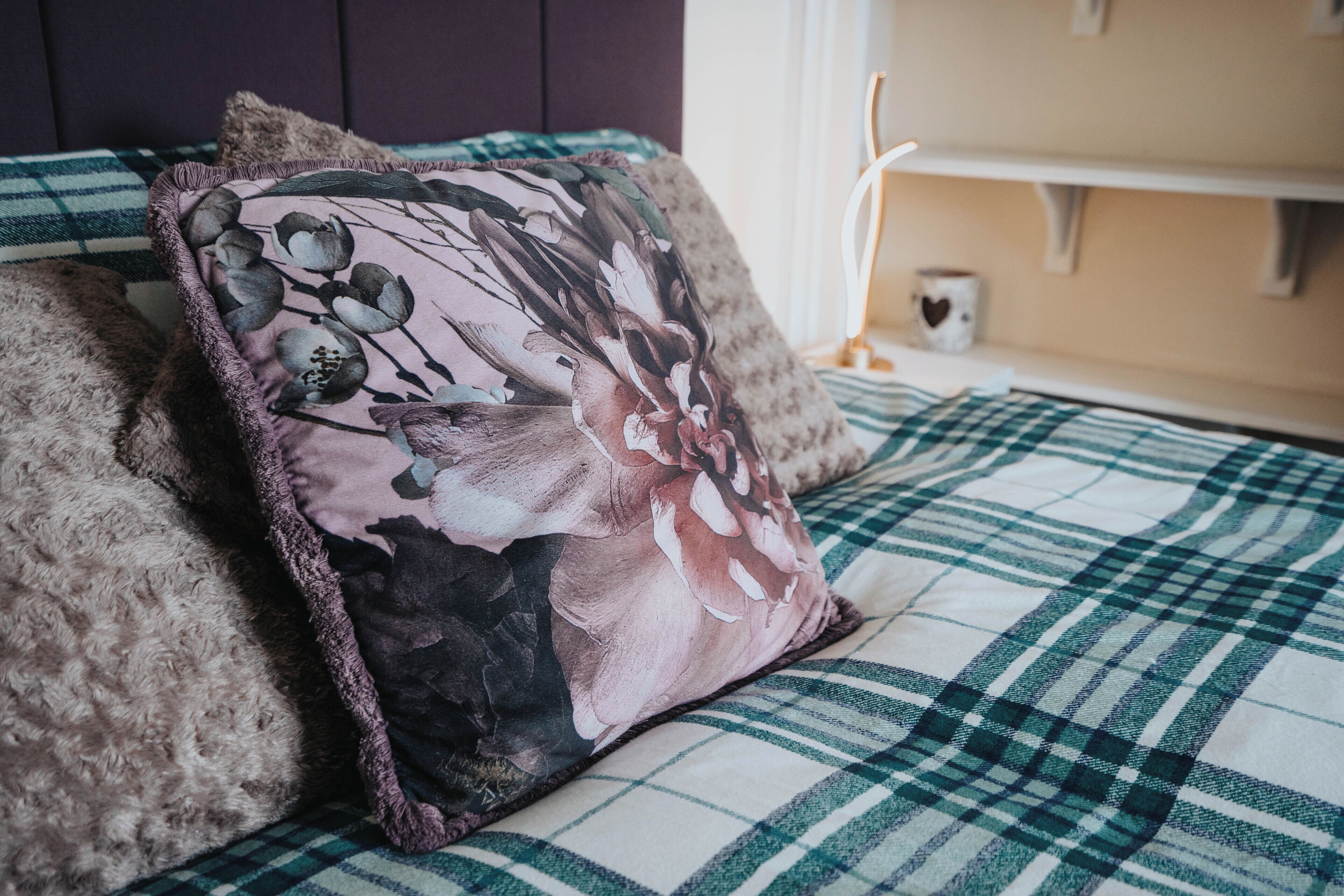 A bed with a floral pillow and a plaid blanket.