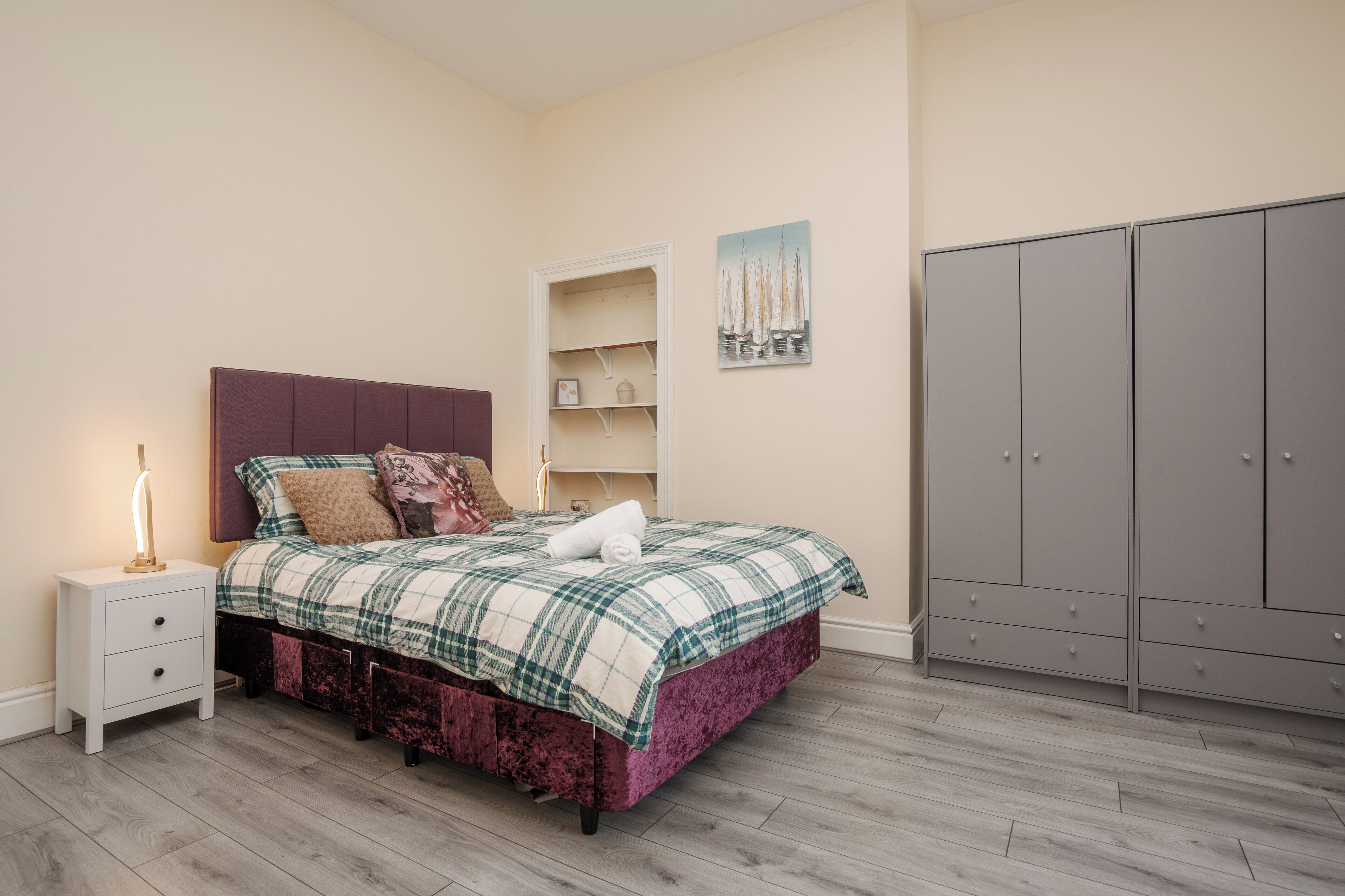 A bedroom with a bed, nightstand, wardrobe, and a wall with a painting.
