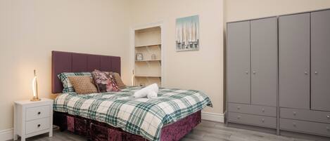 A bedroom with a bed, nightstand, wardrobe, and a wall with a painting.