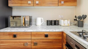 Eine moderne Küche mit Holzausstattung, einer Marmorarbeitsplatte, einer Kaffeemaschine, Aufbewahrungsbehältern für Tee und Kaffee sowie einem integrierten Geschirrspüler.
