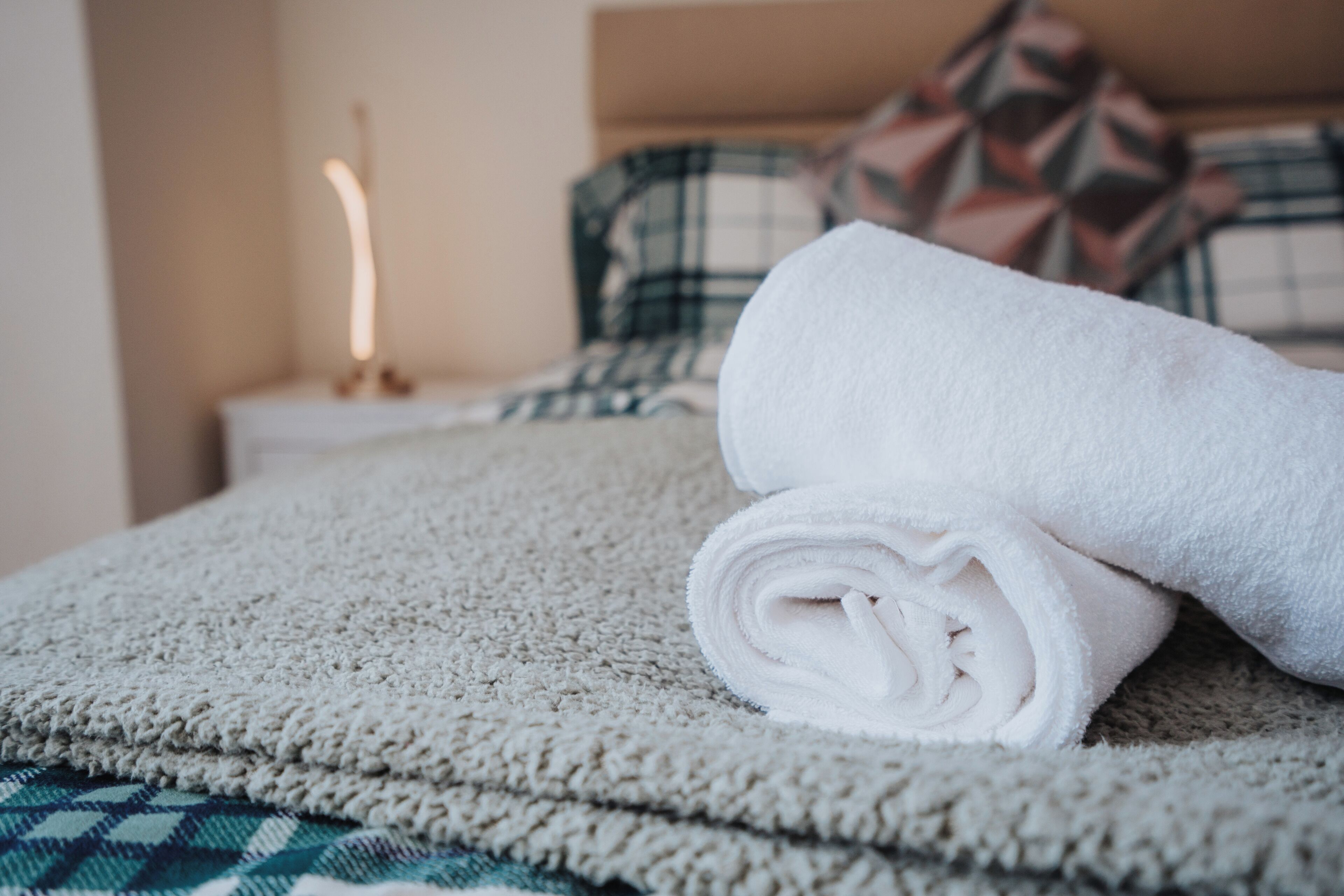 A neatly made bed with a rolled white towel and a patterned blanket.