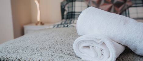 A neatly made bed with a rolled white towel and a patterned blanket.