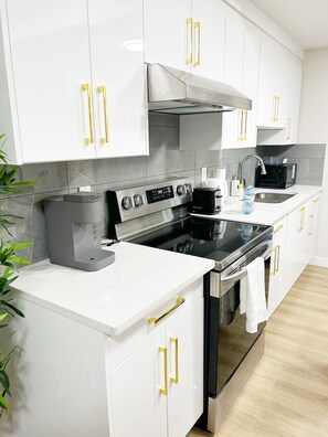 Een moderne keuken met witte kastjes, roestvrijstalen apparatuur en gouden knoppen.