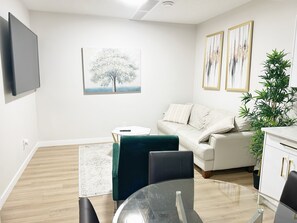 A modern living room with a sofa, a glass table, a green chair, a white cabinet, and a large plant. - Beautiful and Cozy brand new 2-bedroom basement suite with WiFi in Edmonton (Edmonton)