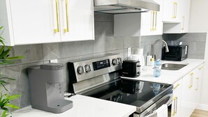 A modern kitchen with white cabinets, stainless steel appliances, and gold handles.
