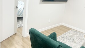A living room with a flat-screen TV mounted on the wall, a green sofa, and a patterned rug.
