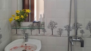 A bathroom with a white sink, a mirror, a shower, and a decorative tree mural on the wall. - Cong Man Homestay - Cham Island (Da Nang)