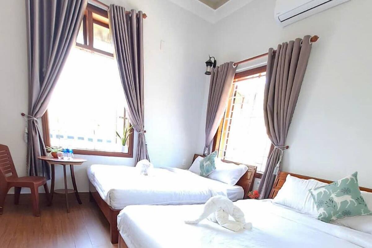 A hotel room with two beds, a small table, a chair, and a potted plant.