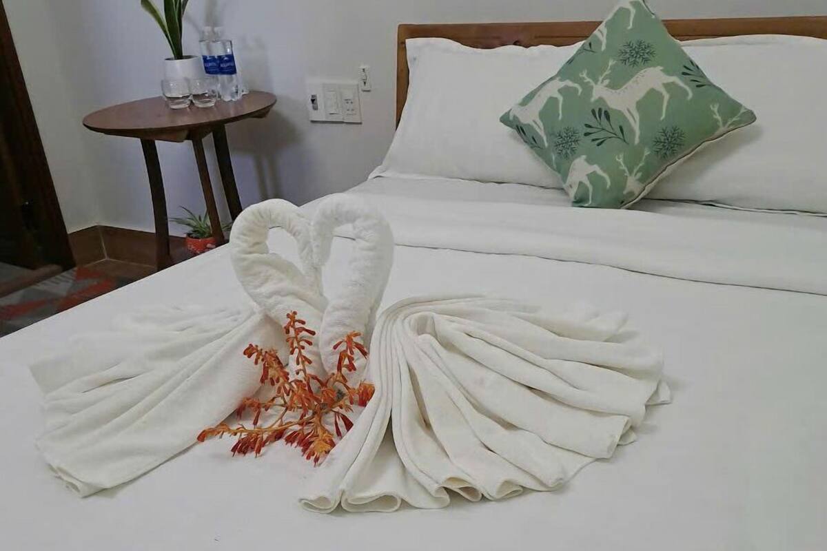 A neatly made bed with a heart-shaped towel arrangement and a decorative pillow.