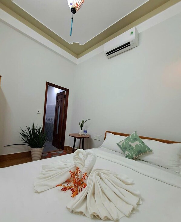 A hotel room with a bed, a potted plant, a small table, and an air conditioning unit. - Cong Man Homestay - Cham Island (Da Nang)