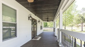 Een overdekte veranda met een houten vloer, witte muren en een witte balustrade.