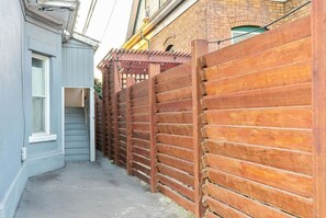 A narrow alleyway with a wooden fence on one side and a brick building on the other. - Beehive Bungalow | Central Location (Salt Lake City)
