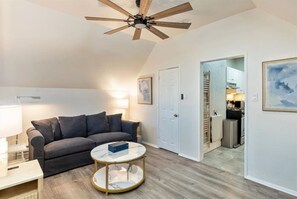 A living room with a grey sofa, a round coffee table, a ceiling fan, and a kitchen visible through an open door. - Beehive Bungalow | Central Location (Salt Lake City)