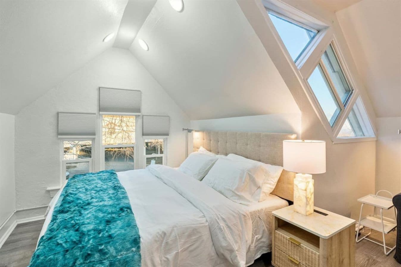 A bedroom with a large bed, a nightstand, a lamp, and a window.