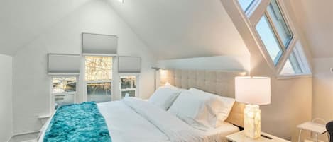 A bedroom with a large bed, a nightstand, a lamp, and a window.