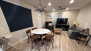 Ein modernes Wohnzimmer mit einem runden Esstisch, Holzstühlen, einer Couch, einem Fernseher und einem Deckenventilator.
