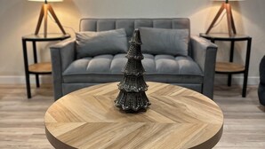 Ein runder Holztisch mit Metallfuß, ein dekorativer Weihnachtsbaum und zwei Nachttischlampen auf passenden Nachttischen.