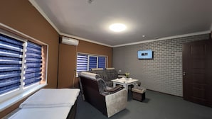 Een kamer met een bank, een tafeltje met een vaas, een aan de muur bevestigde televisie en een deur.