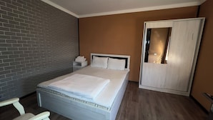 Een netjes opgemaakt bed met witte lakens, een houten hoofdbord en een nachtkastje met een lamp.