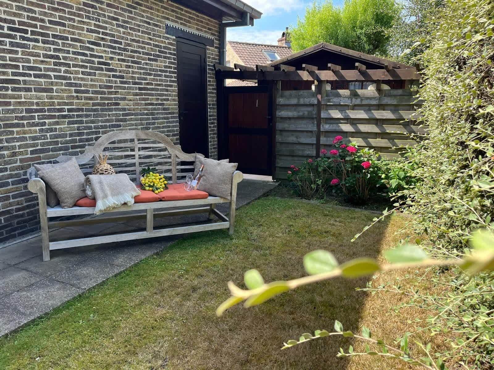 A wooden bench with cushions and a basket of lemons in a garden area with a brick wall and wooden fence.