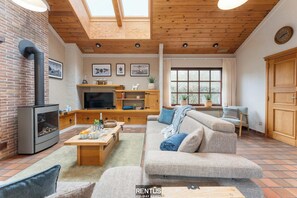 Un salon chaleureux avec une cheminée, un plafond en bois et une grande fenêtre.