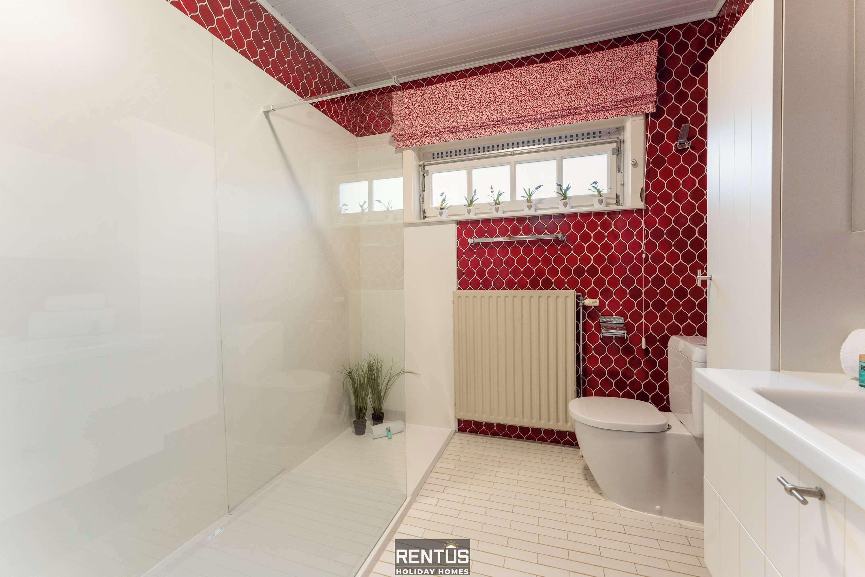 Ein Badezimmer mit Dusche, Toilette und Waschbecken, mit einer roten Wand mit Muster und weißen Fliesen.