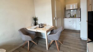 Una cocina moderna con armarios blancos, una mesa de comedor con dos sillas y un televisor a la derecha.