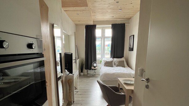 Una habitación funcional con kitchenette, cama, escritorio y silla.