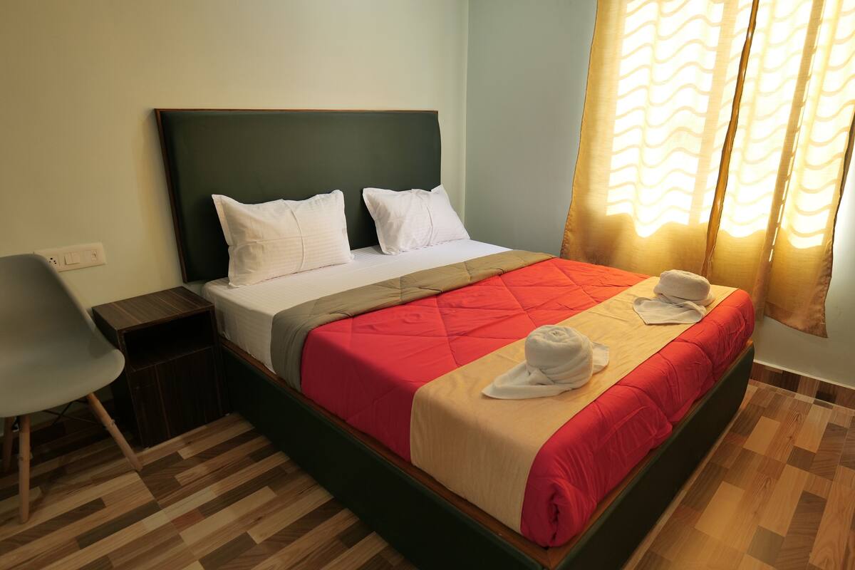 A neatly made bed with a red and beige bedspread, two white pillows, and a towel on the bed.
