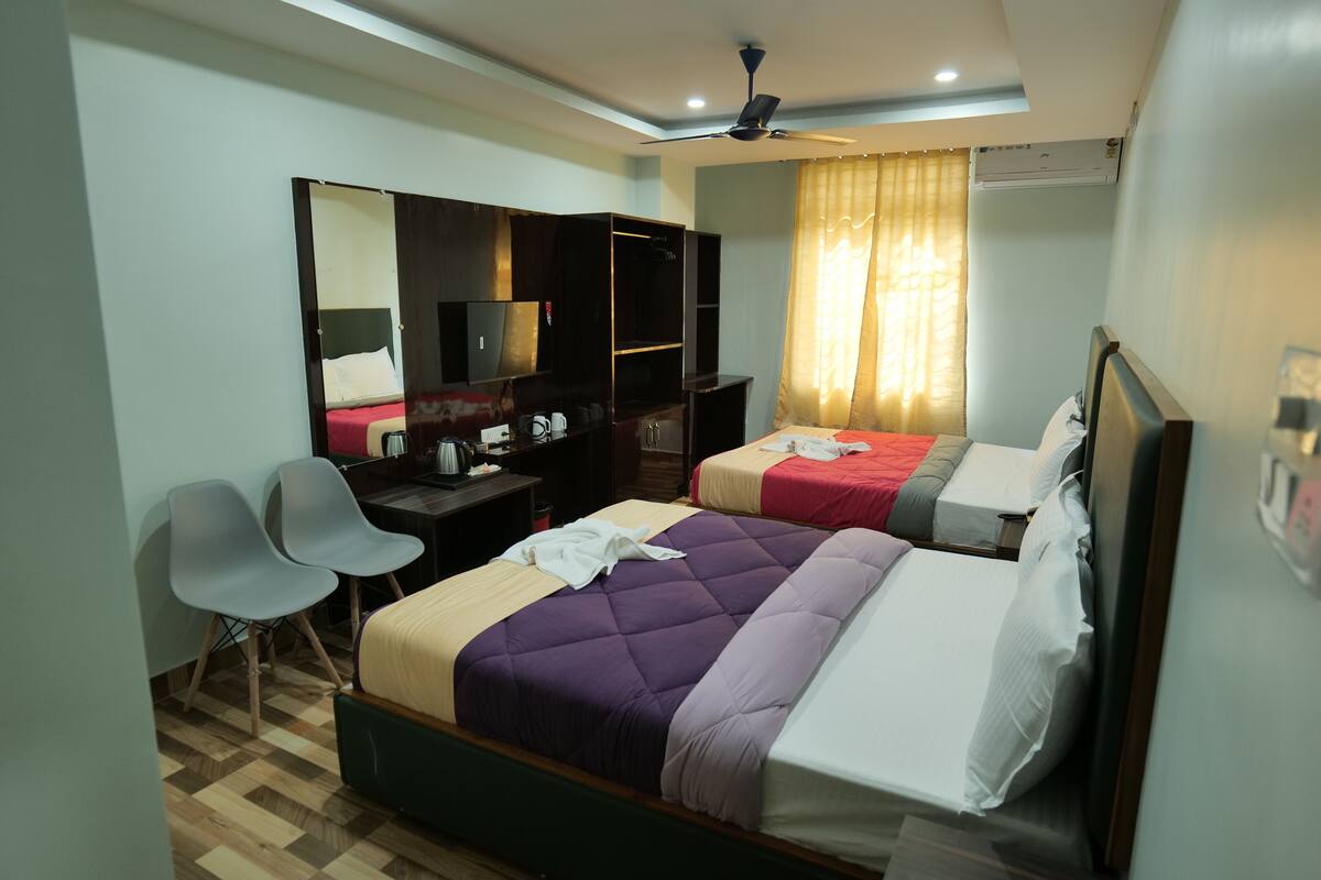 A hotel room with two beds, a desk, a chair, a wardrobe, and a ceiling fan.