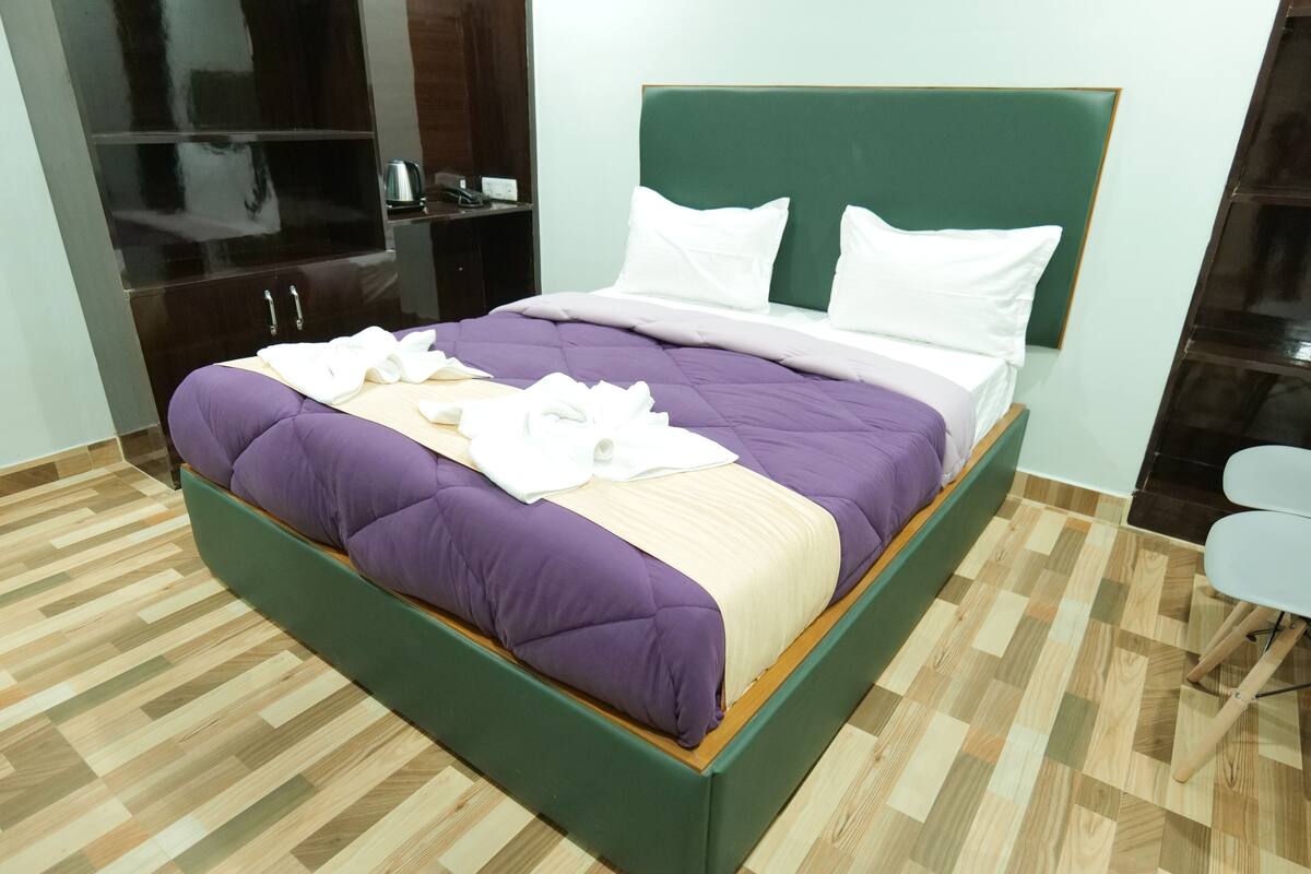 A neatly made bed with a green headboard, a purple and beige bedspread, and white pillows.