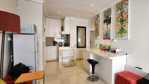 Een moderne keuken met witte kasten, een eethoek met een rode bank en een bar met een kruk.