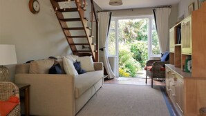 A living room with a sofa, a wooden staircase, a bookshelf, and a view of greenery outside. - Thin End (Seaview)