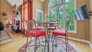 A dining area with a round table and red chairs, a fireplace, and a large window with a view of trees. - Spacious and comfy 4 Bed/3 Full Bath Canton Home! (Canton)