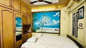 A bedroom with a bed, wooden wardrobe, ceiling fan, and a large beach-themed painting.