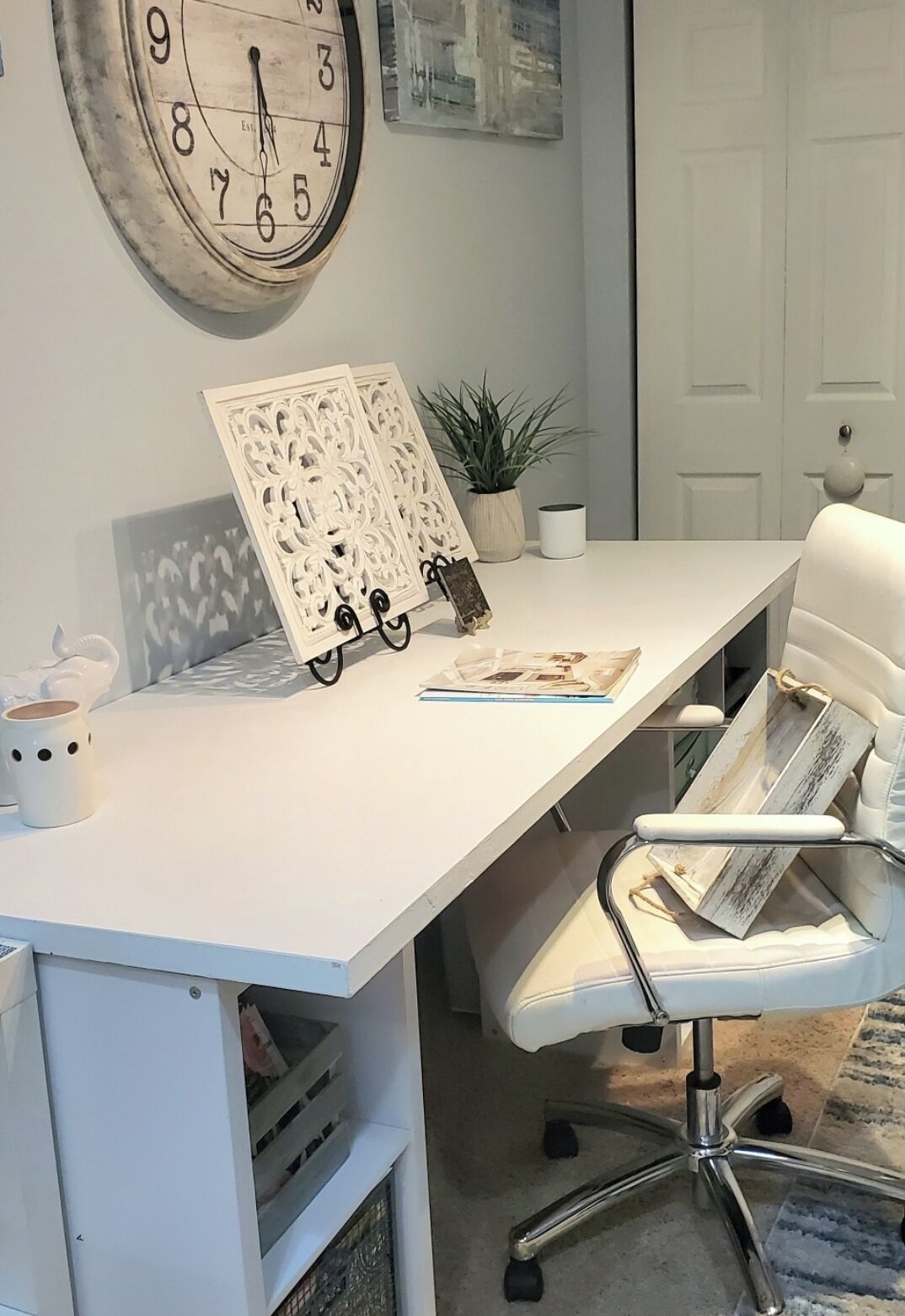 Een wit bureau met een klok, een witte stoel en een potplant.