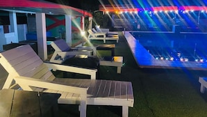 Un área de piscina al aire libre con sillas de descanso y una zona de estar cubierta.