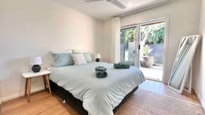 A bedroom with a bed, nightstands, a ceiling fan, and a sliding glass door leading to a balcony.