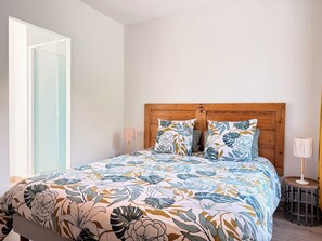 A bedroom with a wooden headboard, floral bedding, a bedside lamp, and a view of a glass door.