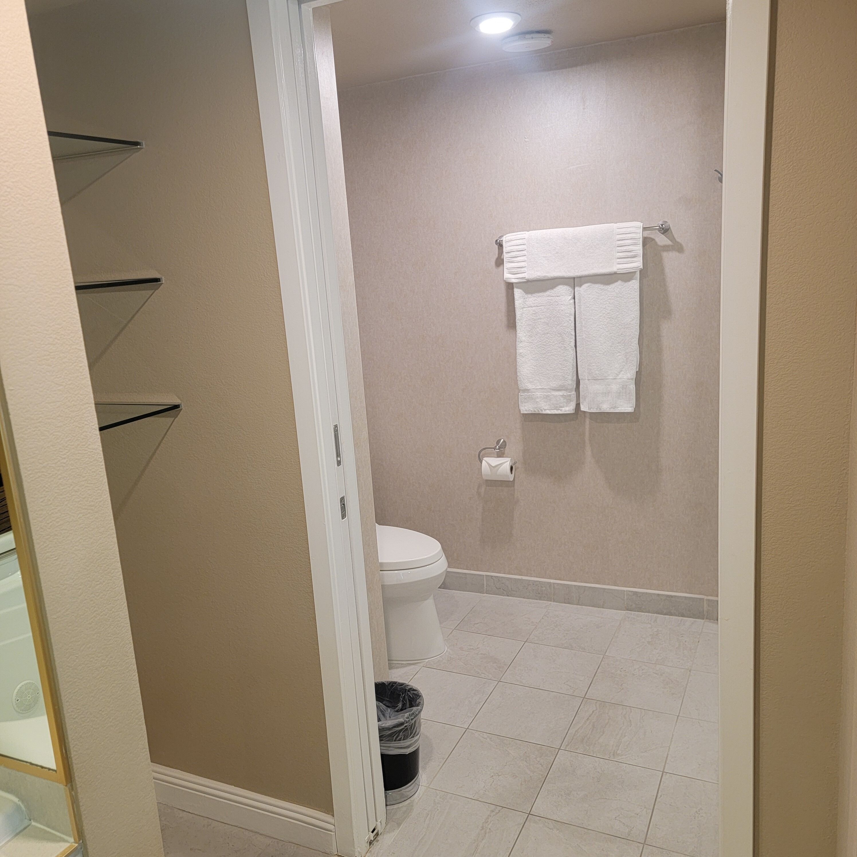 Une salle de bain équipée de toilettes, d’une poubelle et d’un porte-serviettes avec deux serviettes.