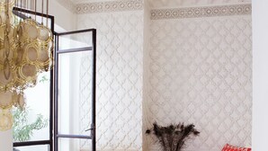 A room with a glass table, white furniture, patterned wallpaper, a decorative vase, and a red and white throw blanket. - Ptit Habibi (Marrakech)